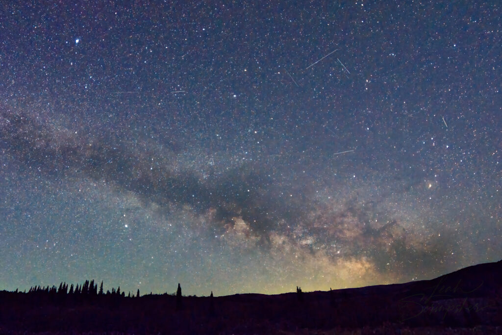 Milky Way arching across the night sky above Moose Ponds in Idaho's South Hills. Dark dust lanes divide the bright core of the galaxy while marsh grasses and still water lie in shadow below.