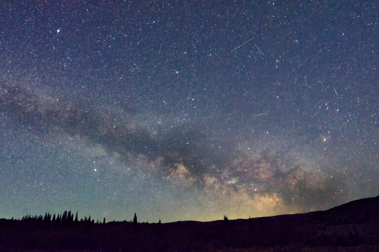 Milky Way arching across the night sky above Moose Ponds in Idaho's South Hills. Dark dust lanes divide the bright core of the galaxy while marsh grasses and still water lie in shadow below.