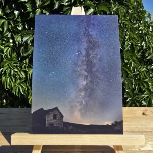 Last Night at the Old Shack postcard displayed on a small wooden easel, image shows the Milky Way over the silhouette of an old shack