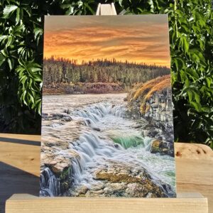 Postcard featuring Sheep Falls Sunset displayed on a small wooden easel, colorful sunset over a waterfall