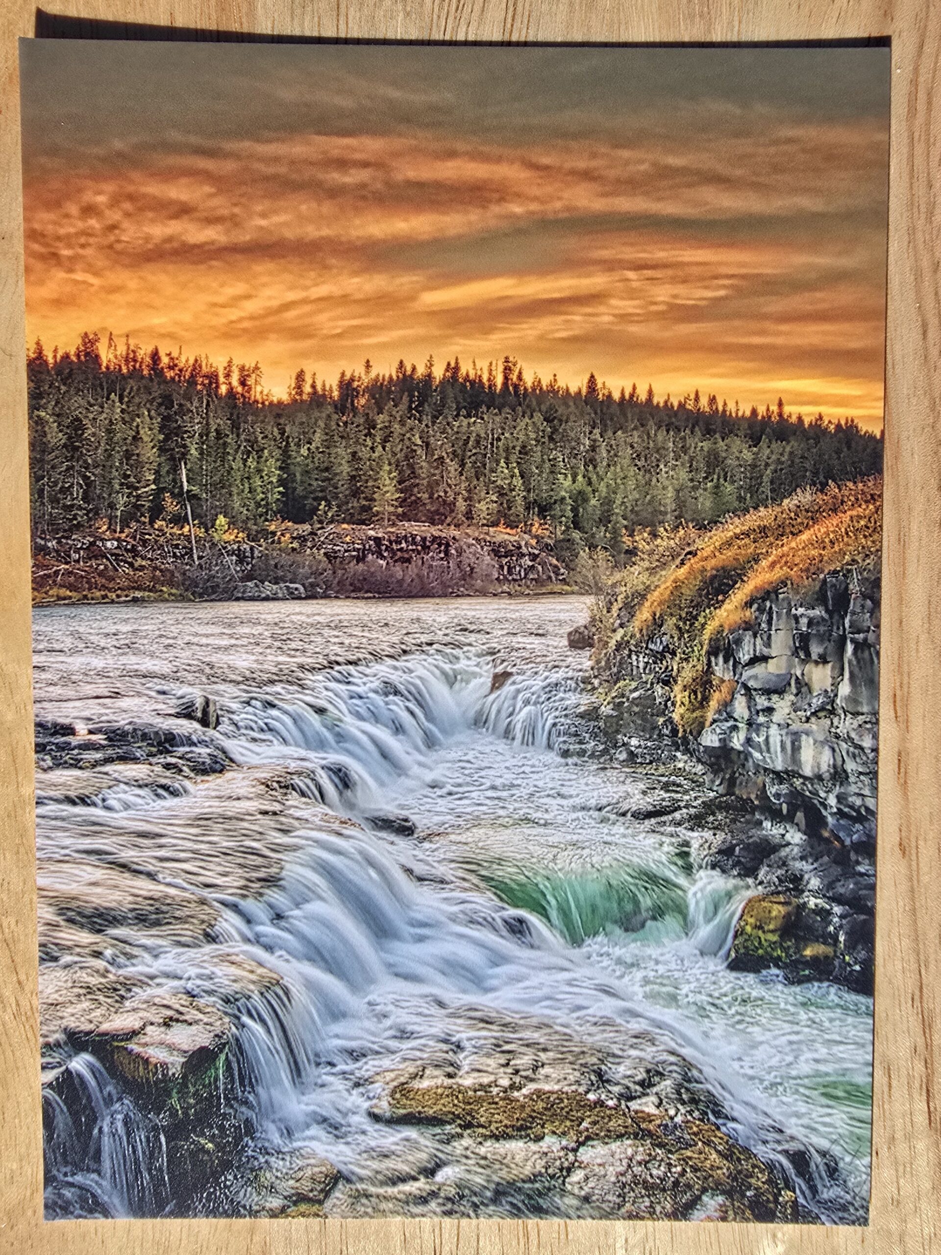 Postcard featuring Sheep Falls Sunset displayed flat on a table, colorful sunset over a waterfall